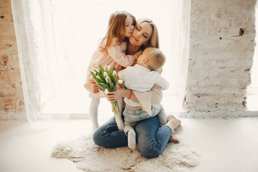 maminka se objímá se svými dětmi a v ruce má kytici tulipánů