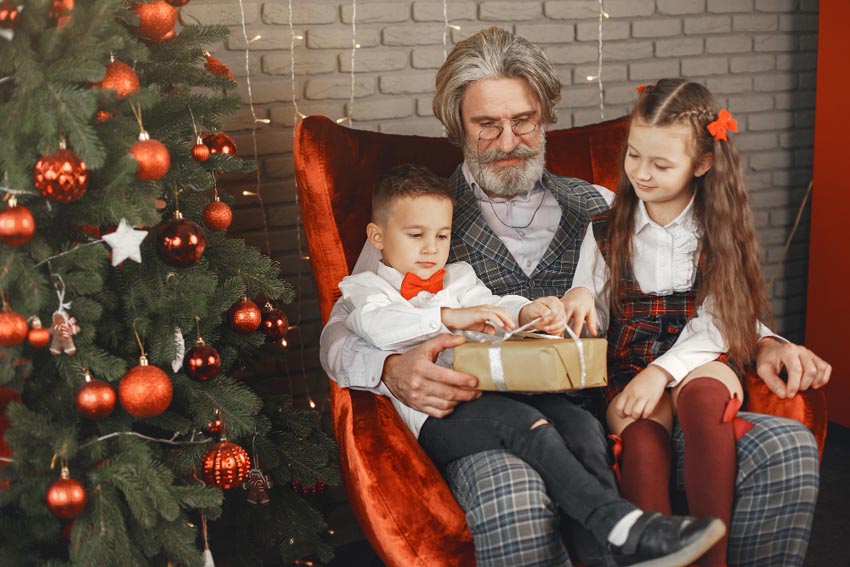 dedko s vnúčatami pri vianočnom stromčeku rozbaľujú vianočný darček